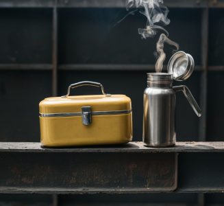 An quaint scene with a lunchbox and thermos on a steel beam