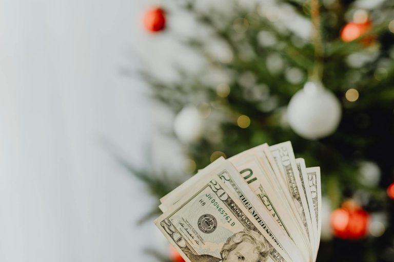 holiday decor with money in hand in foreground; How to Celebrate Without Derailing Your Retirement Goals