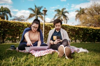 Gen Z couple sitting out on the lawn working; How Gen Z Can Build a Path to Early Retirement