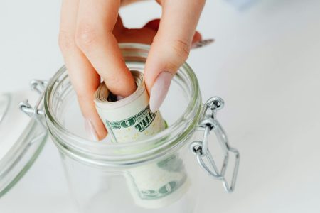 person putting money in an emergency jar; Emergency Fund Reset Is Yours Big Enough