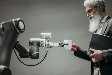 man with coffee cup handed to him by robot; AI Won’t Replace You Will Replace How You Work