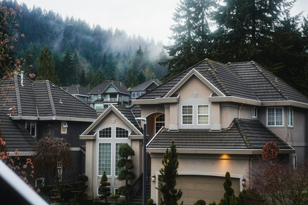 Modern suburban houses with gray roofs surrounded by trees and misty forested hills in the background