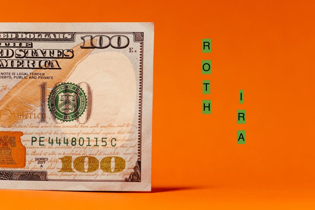 Half of a $100 bill next to green letter tiles spelling ROTH IRA on an orange background