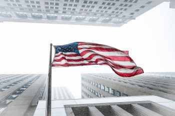 large american flag waving high between tall buildings; What America’s 250th Anniversary Teaches Us About Entrepreneurial Greatness