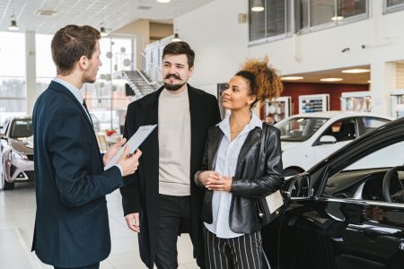 Couple speaking with car dealer in modern sales floor and deciding on which car to buy; Car Buying Process