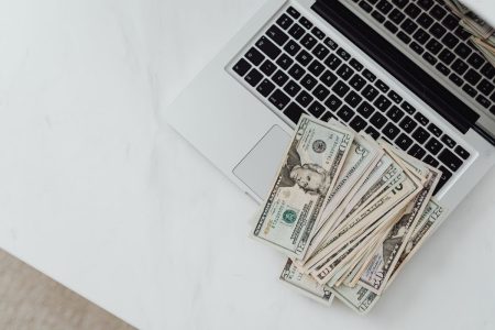 Image of laptop sitting on white desk while cash lays on top of keyboard; build website passive income