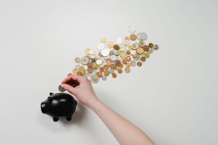 A hand dropping a coin into a piggy bank beside a spread of coins, representing steady retirement saving