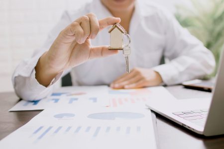 a person holding a little house between their fingers; American Dream Owning a Home Worth It?