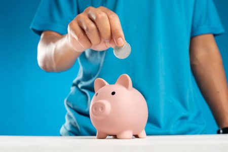 man in turquoise shirt putting money in pink piggy bank
