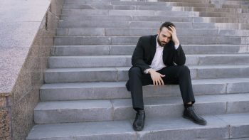 Shows a disheartened man on gray steps head in hand;