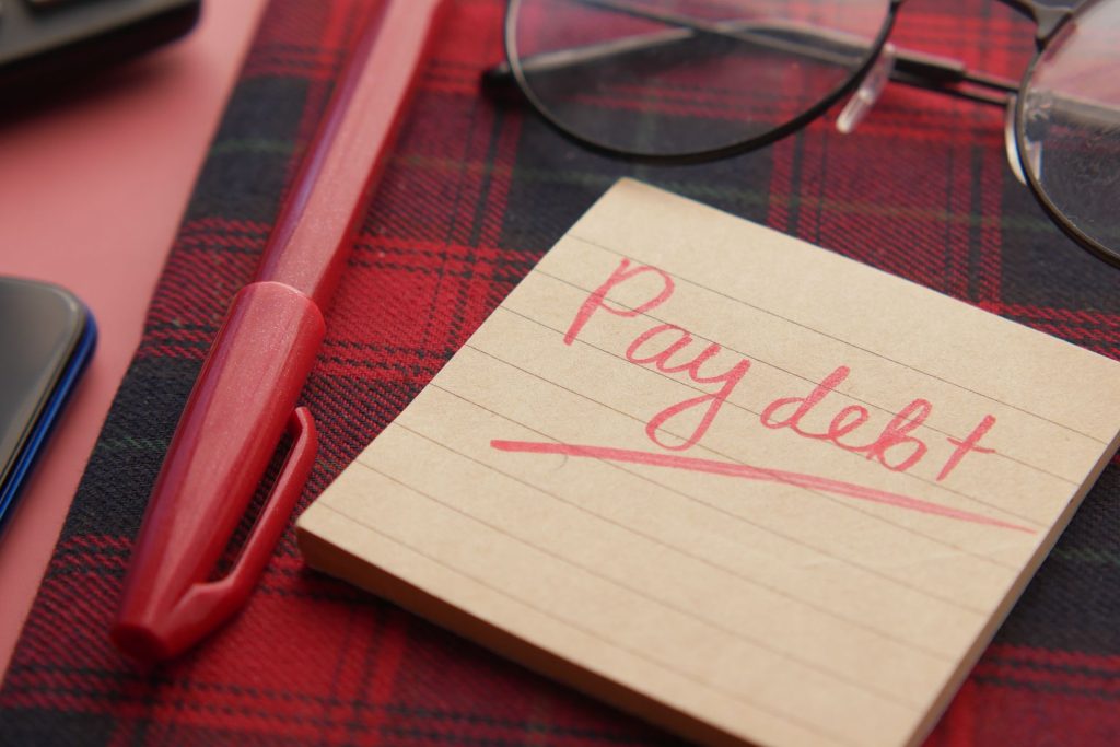 a sticky note that says to pay debt on a plaid background